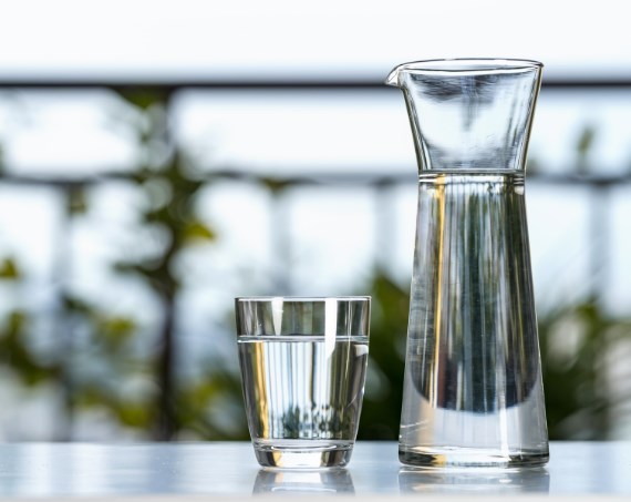 Glas Wasser neben Karaffe, die mit Wasser gefüllt ist vor hellem Hintergrund