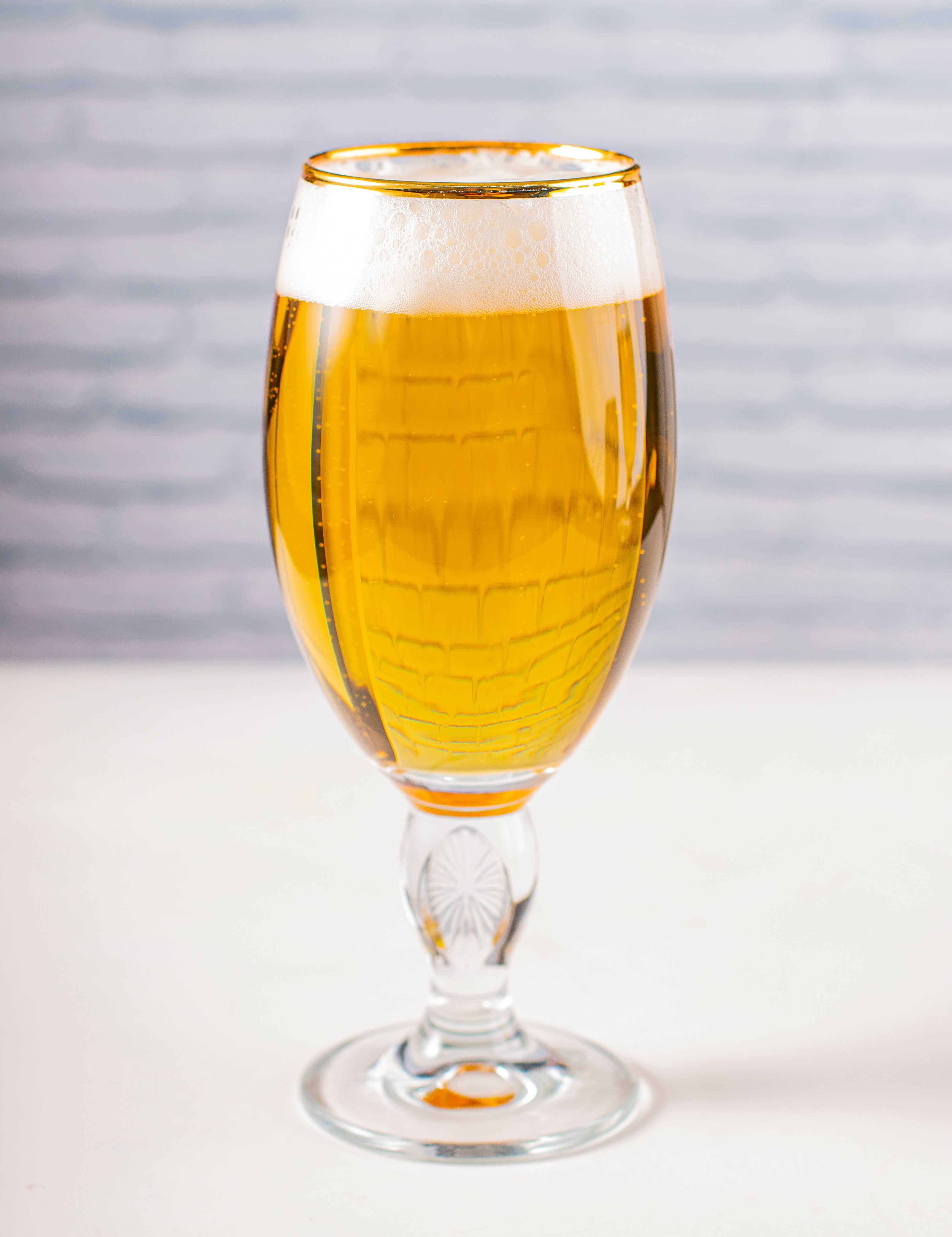 Ein Glas mit Bier und leichtem Schaum, das vor einem hellen Hintergrund auf einem glatten Untergrund steht.