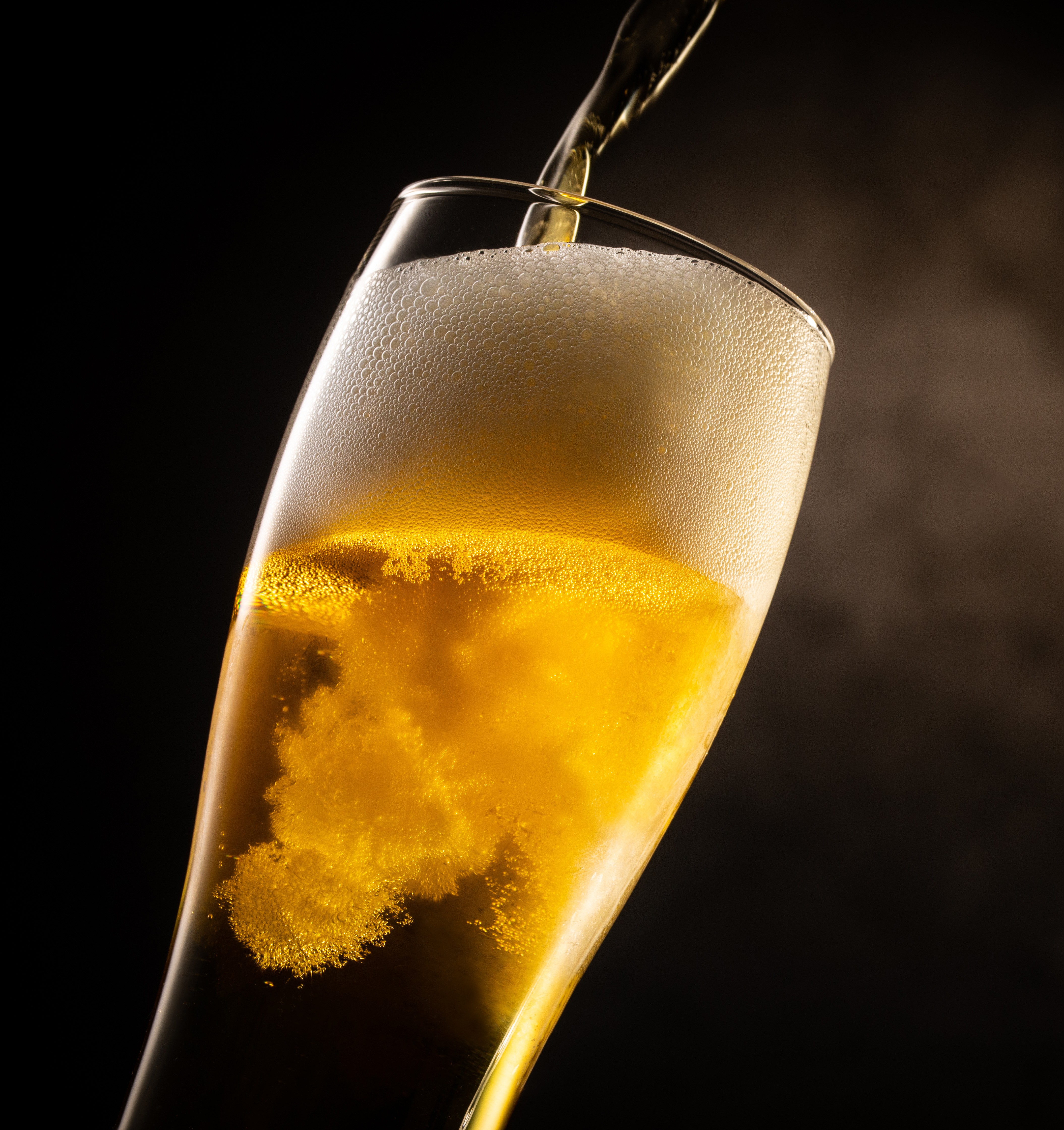 Ein Glas Bier, in das gerade Bier eingegossen wird, wobei der Schaum aufsteigt und die goldene Farbe des Bieres im Licht hervorgehoben wird.