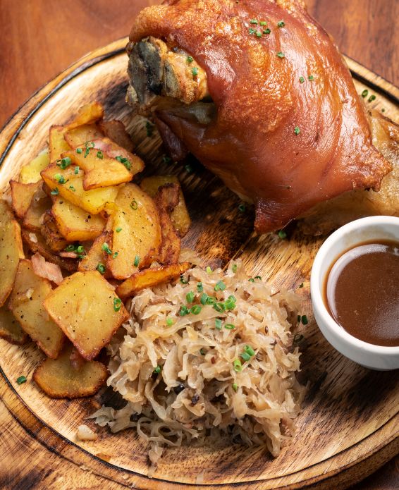 zbrett, serviert mit Bratkartoffeln mit Speck, Sauerkraut und dunkler Bratensoße in einem kleinen Schälchen – garniert mit frischem Schnittlauch.