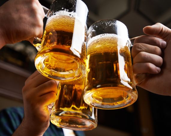 Drei Bierkrüge stoßen an, goldenes Bier mit Schaumkrone in Nahaufnahme.